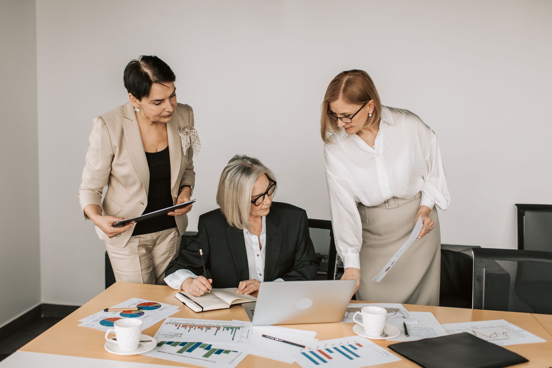 Three businesswomen discussing documents during a meeting in a modern office setting. — 10 Steps regarding how to Create a Bu