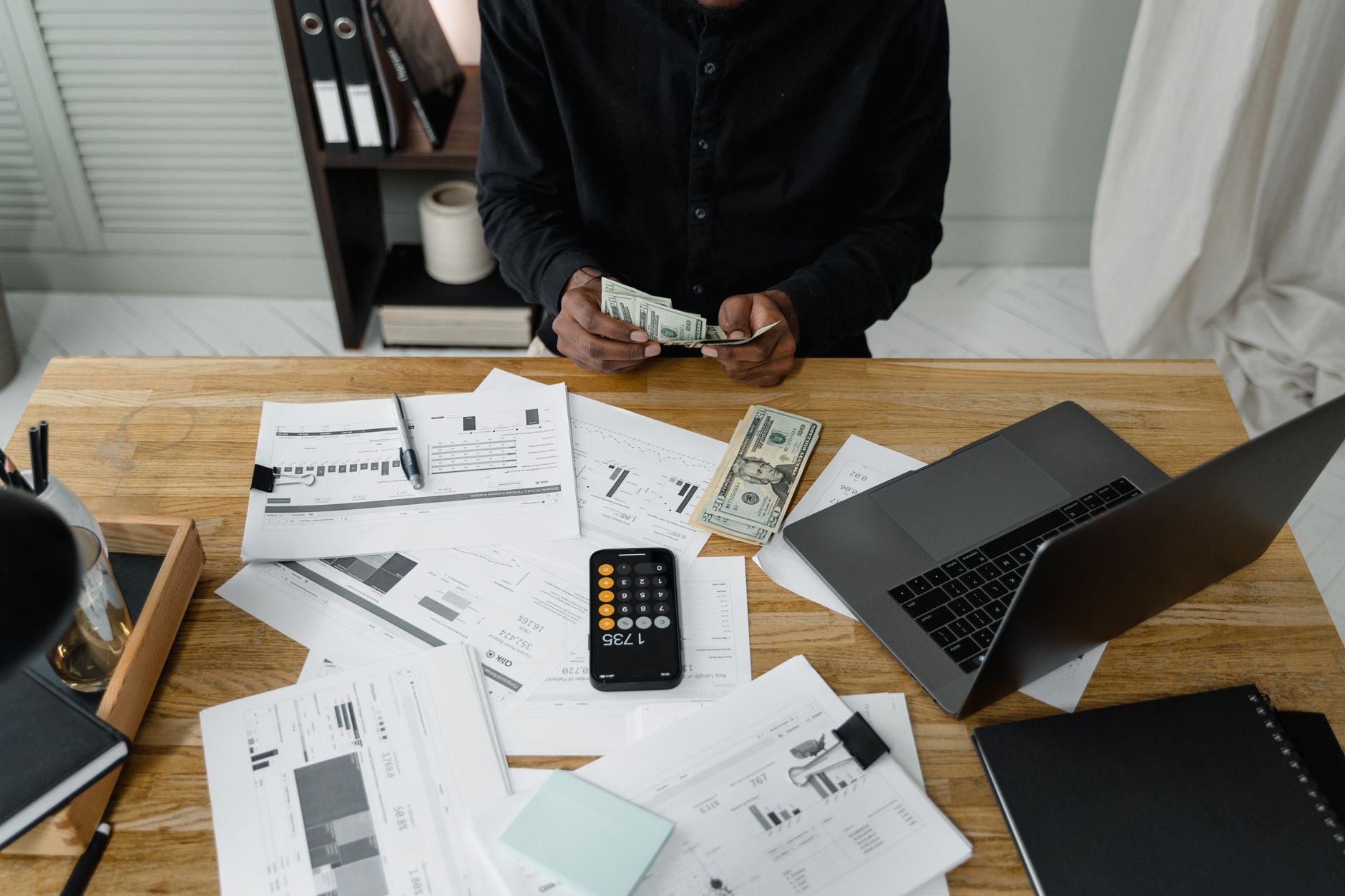 A person counts dollar bills at a desk with a laptop, papers, and calculator. — 9 Errors You Should Avoid While Buying a Term