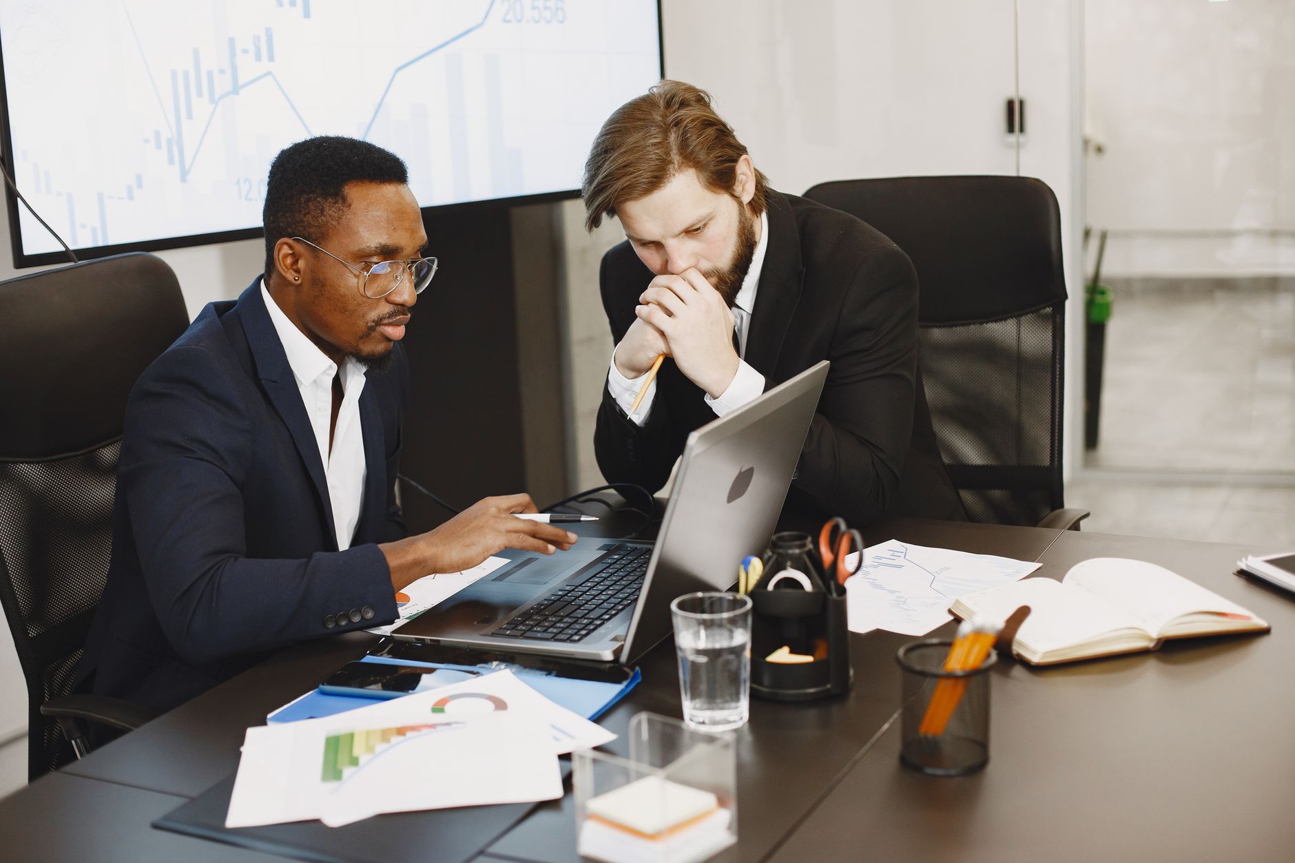 Two businessmen engaged in a strategy meeting with laptops and charts. — Albuquerque car accident: Find more on New Mexico la
