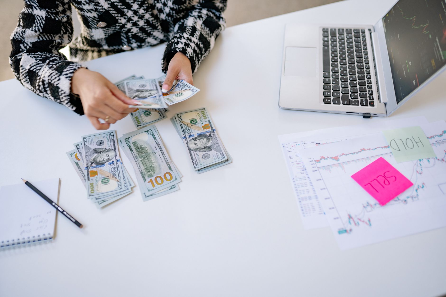 Person counting cash next to laptop and stock market charts on a white table. — Bitcoin and economic freedom