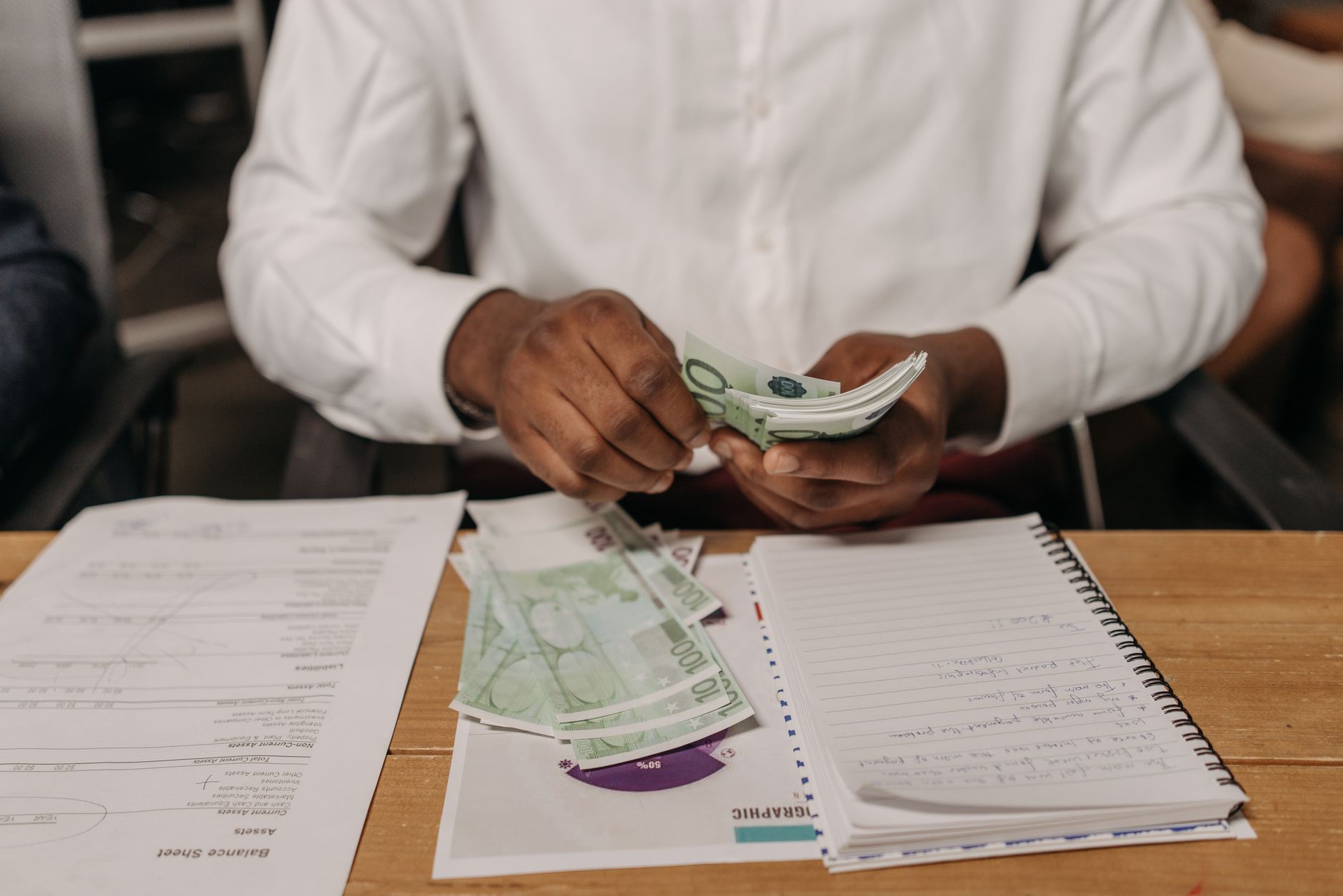 African businessman counting euro bills at a desk with documents and a notebook, highlighting finance theme. — child tax cred