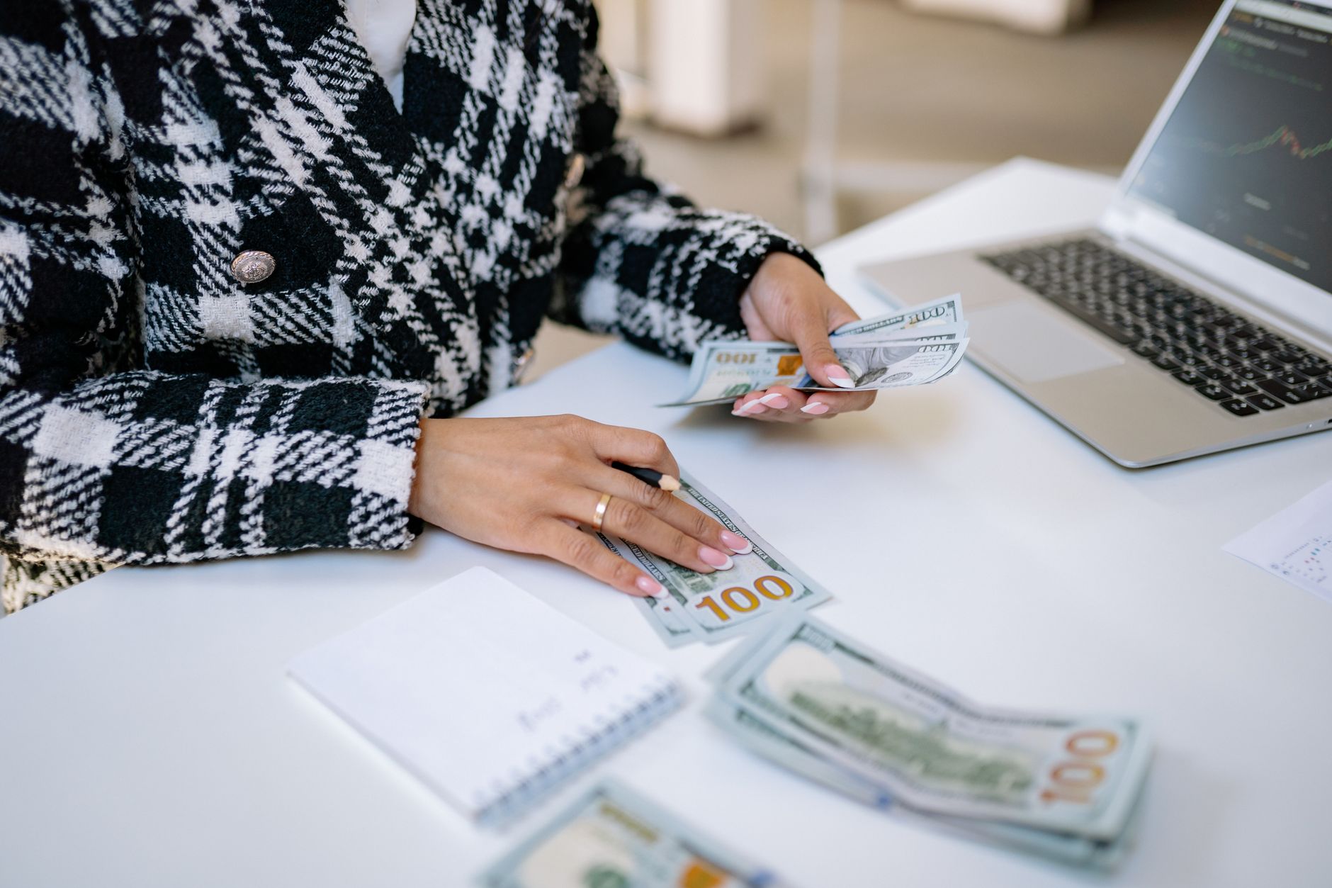 Close-up of a woman counting hundred-dollar bills at a desk with a laptop, focusing on finance and work. — Different Types of