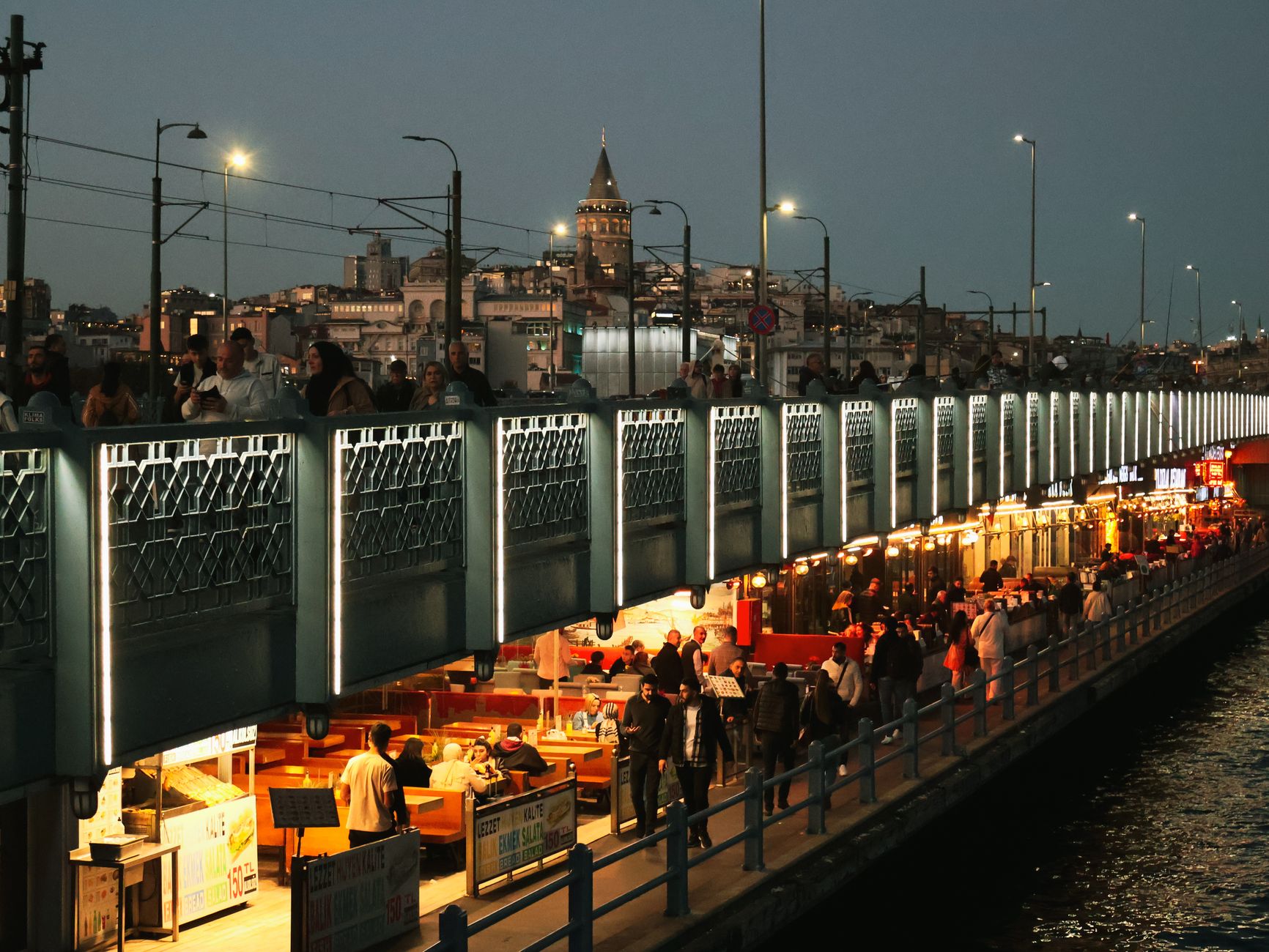 Night view of Galata Bridge bustling with people and distant Galata Tower in Istanbul. — Different ways that you can help you