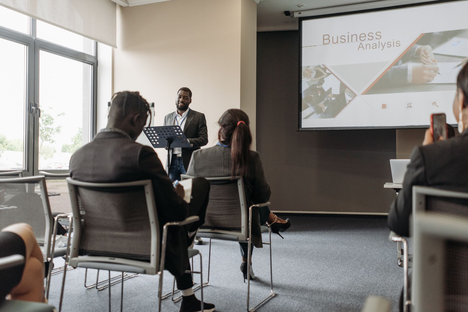 A business professional delivering a presentation in a conference room with diverse attendees. — Get the landscape design for