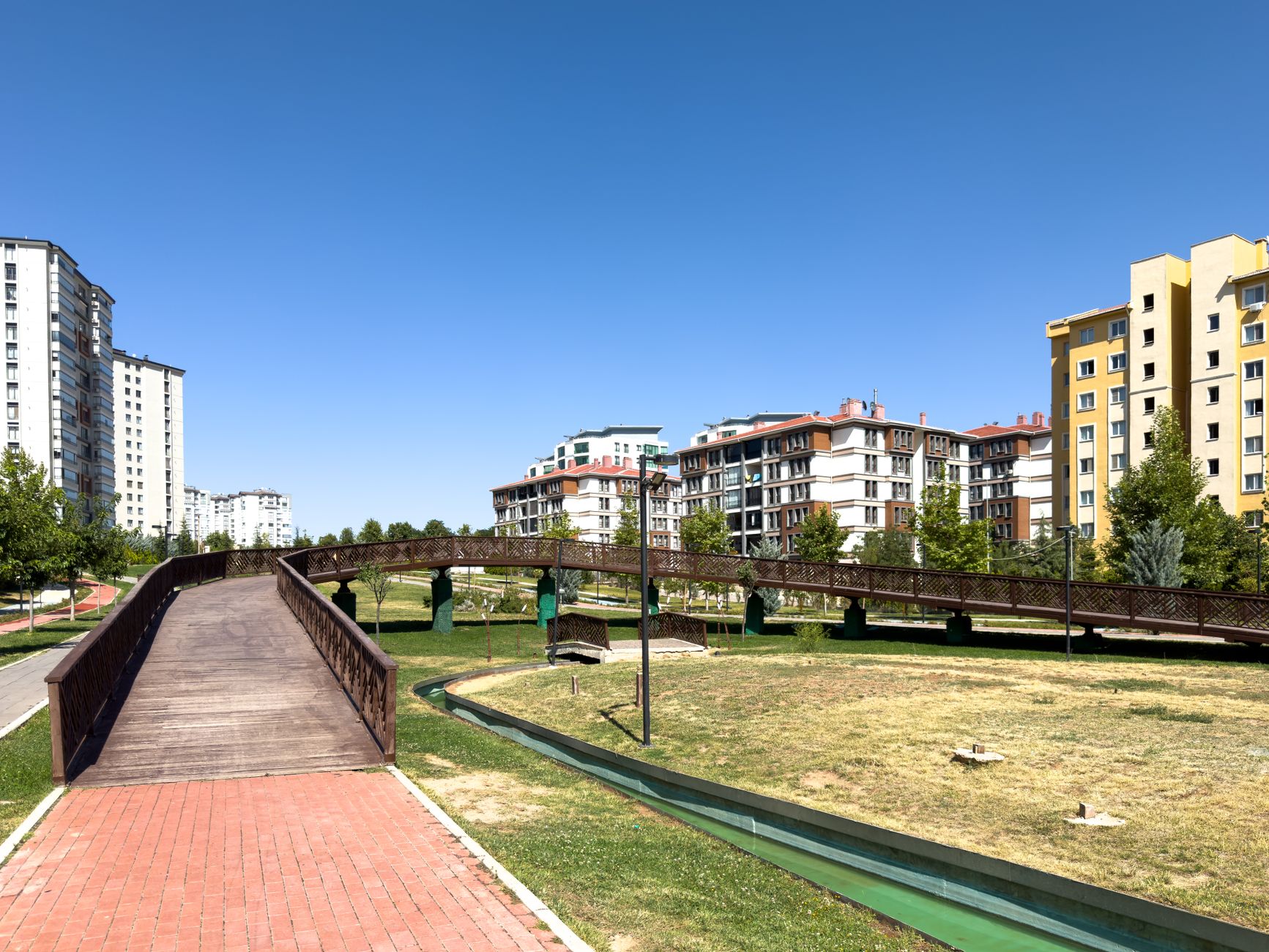 A sunny day in an urban park with modern buildings and a wooden bridge in Elâzığ, Türkiye. — Greater Options for the best of