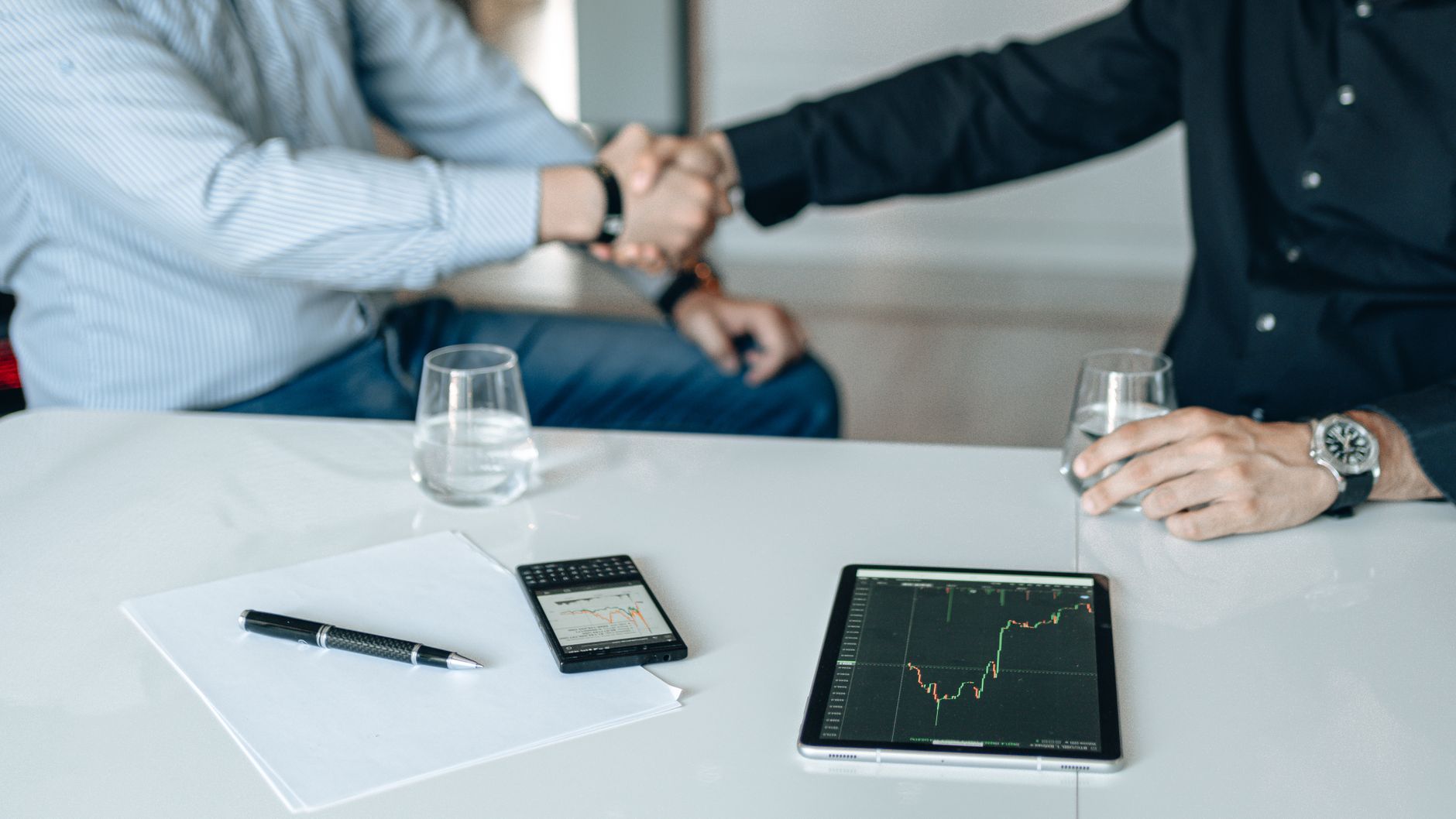 Business meeting with handshake and financial analysis displayed on a tablet. — How are Shipping Pallets Used?