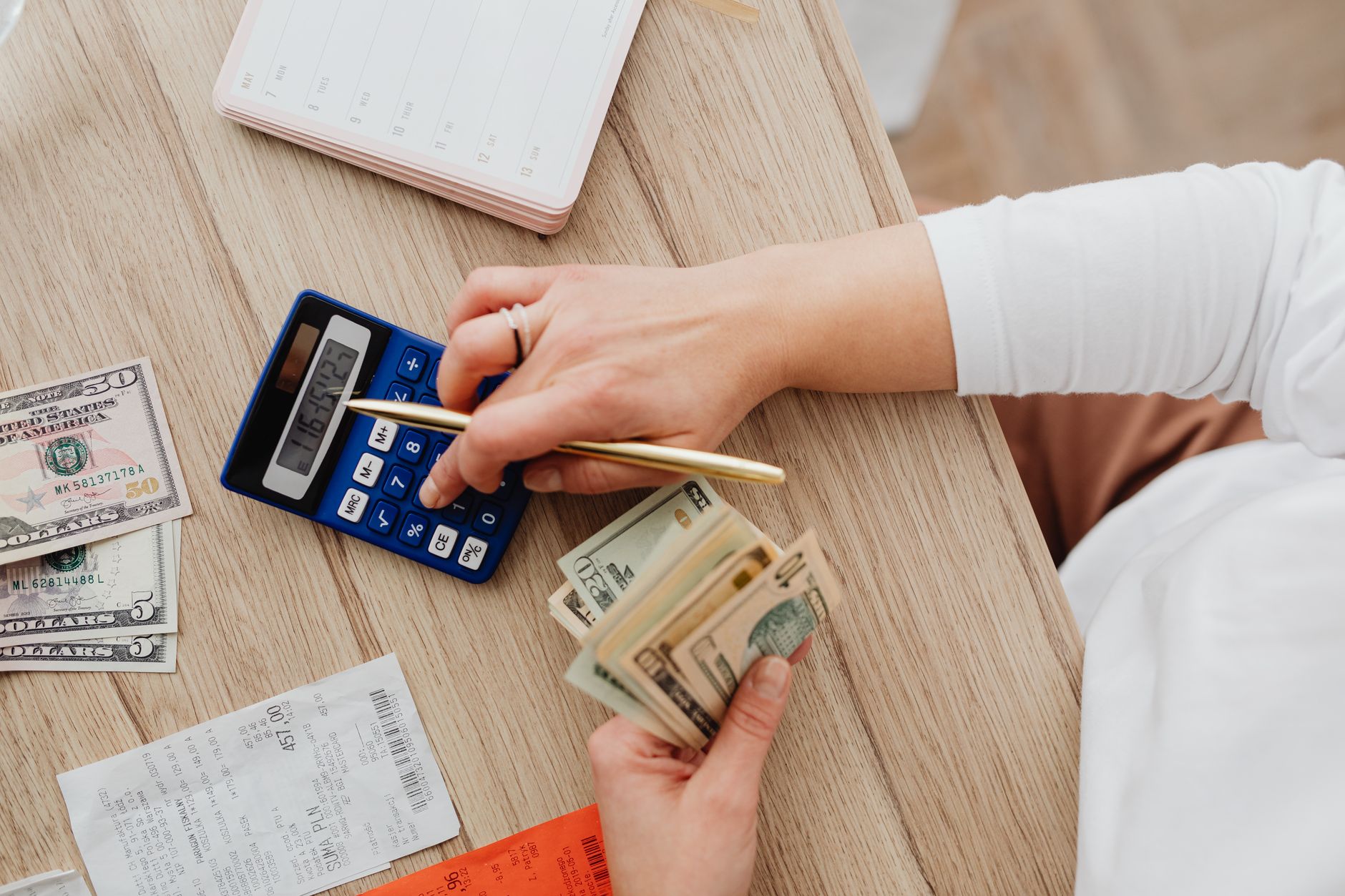 Person using a calculator and counting cash on a wooden table with receipts. — How Can An Online Portal Help You Find The Mos