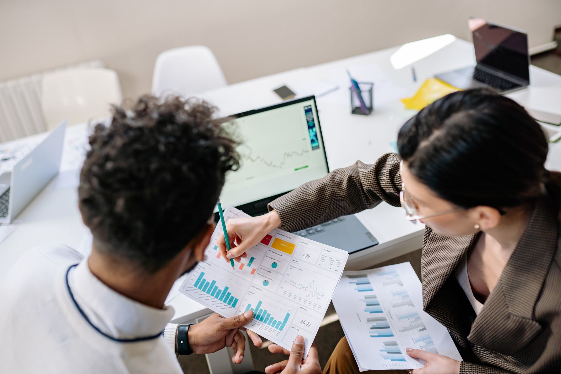 Two colleagues in a meeting room discussing financial charts and graphs on a laptop and paper. — How can you invest on crypto