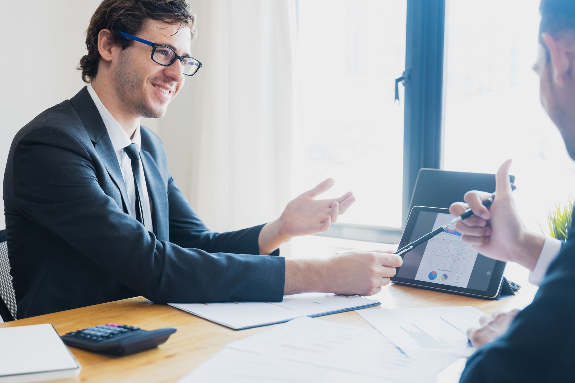 Two businessmen in formal attire discussing a business report in an office setting with a tablet. — How paid ads are going to