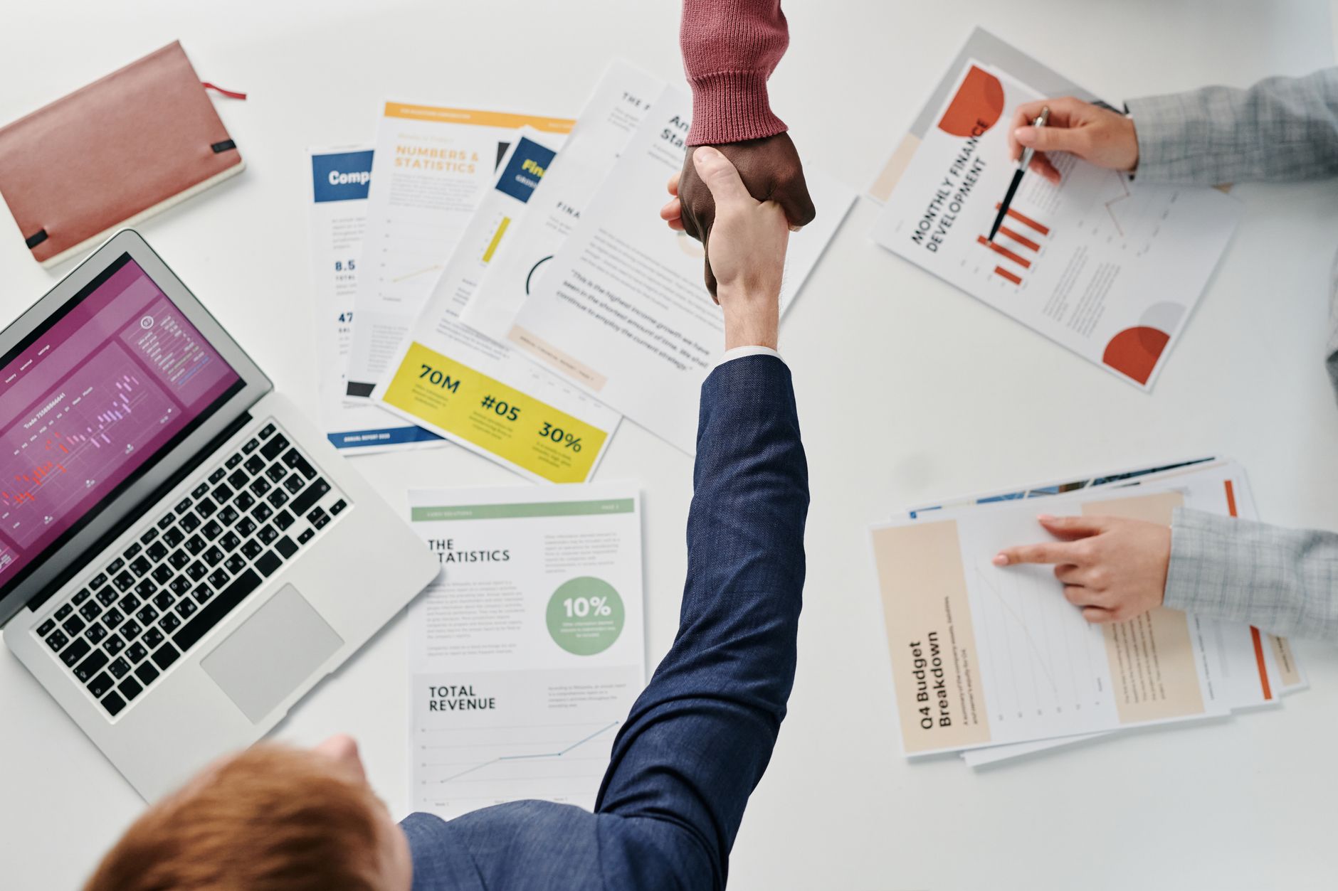 Business professionals engaging in a handshake over a desk filled with financial documents and a laptop. — How religion can a