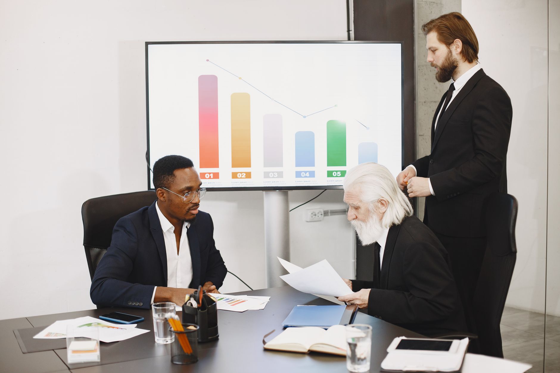 Three businessmen discussing financial data in a modern office setting with charts. — How to reassure staff after a break-in