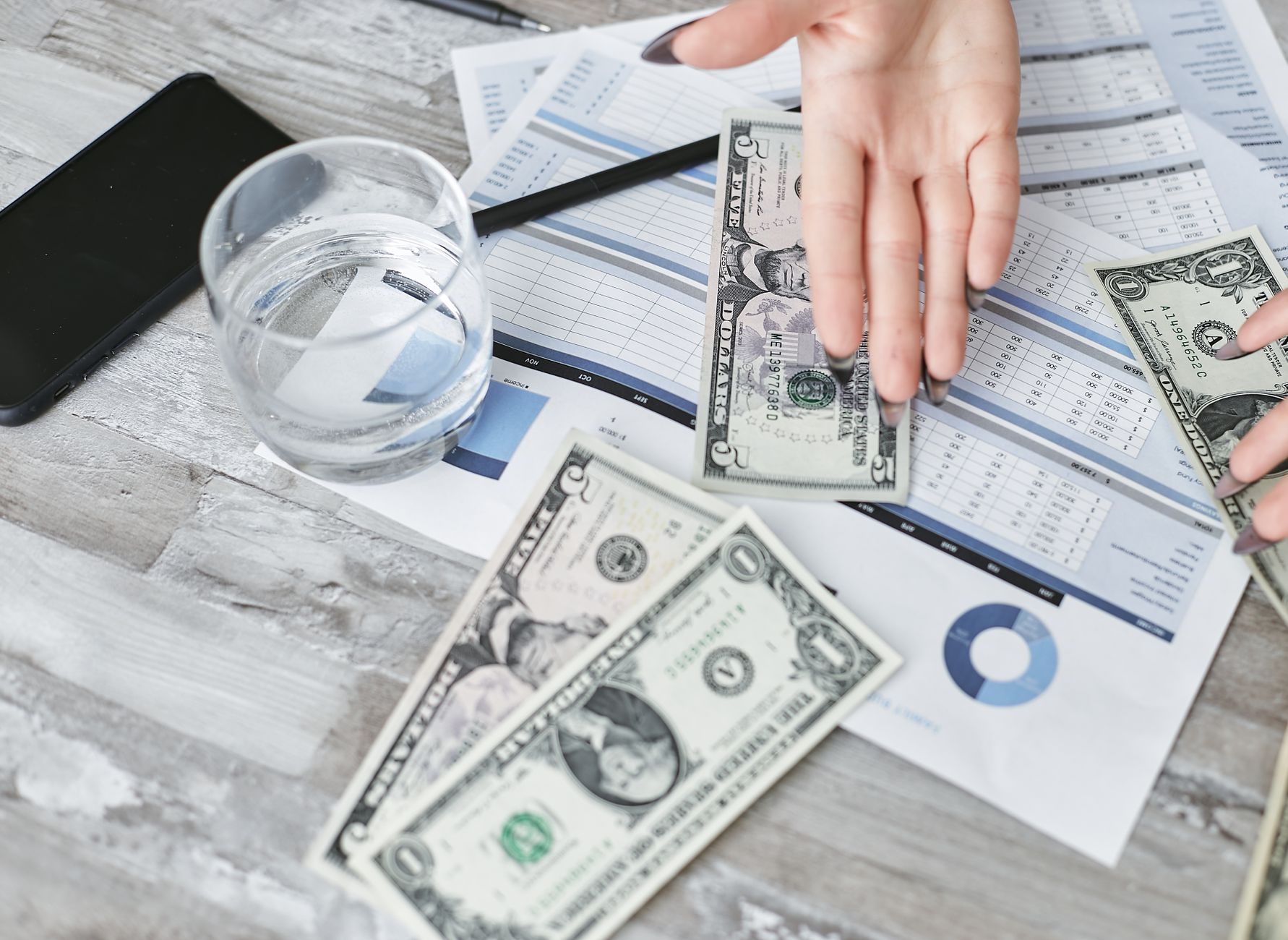 A top view of financial documents with dollar bills and a glass of water, emphasizing budgeting. — How to Set Up the Small Bu