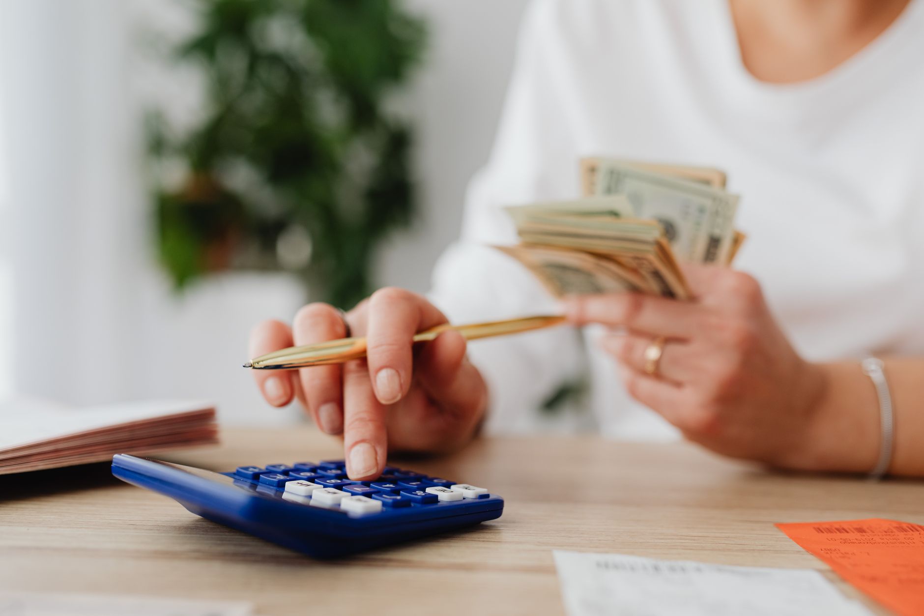 A person sits at a desk calculating finances using a calculator and holding cash. — Searching For That Appropriate Business F