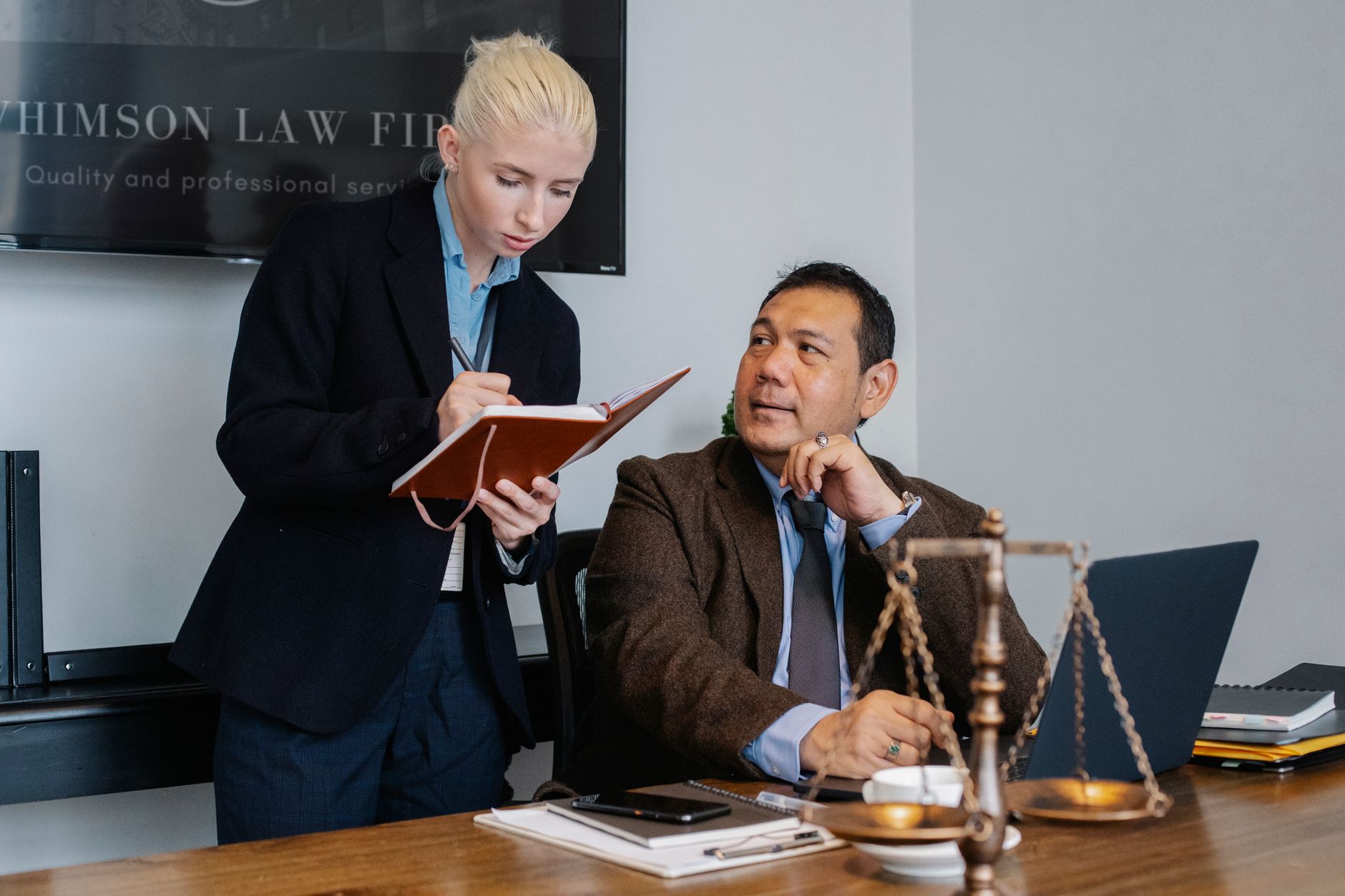 Young female secretary in formal clothes taking notes in notebook and taking to serious Asian male manager while working in l