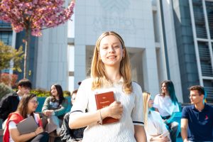 Happy university students socializing on campus, with a focus on a smiling young woman holding a book. — Unleashing t