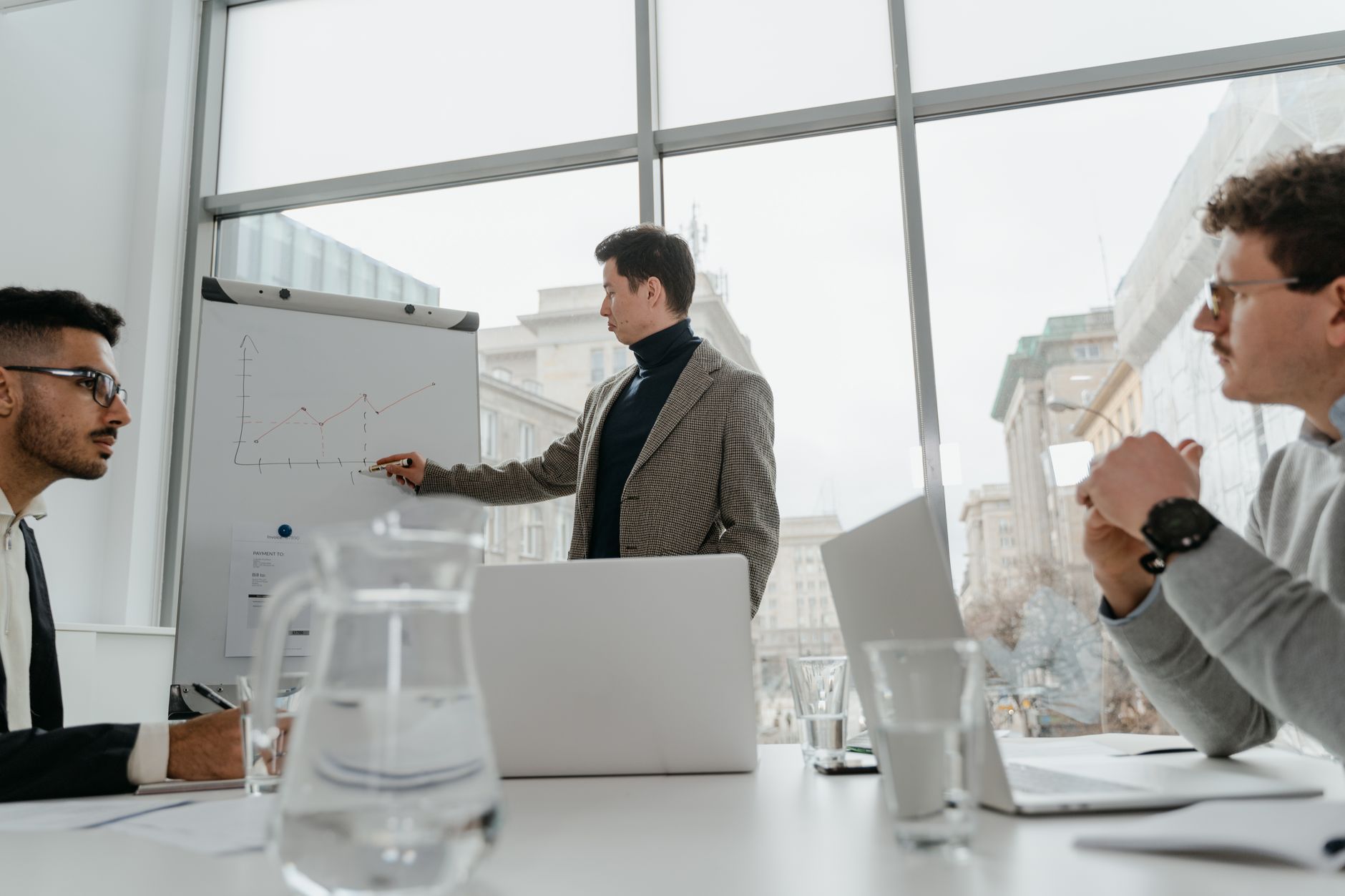 Professionals engaged in a collaborative business meeting with charts and laptops in a modern office setting. — Upgra