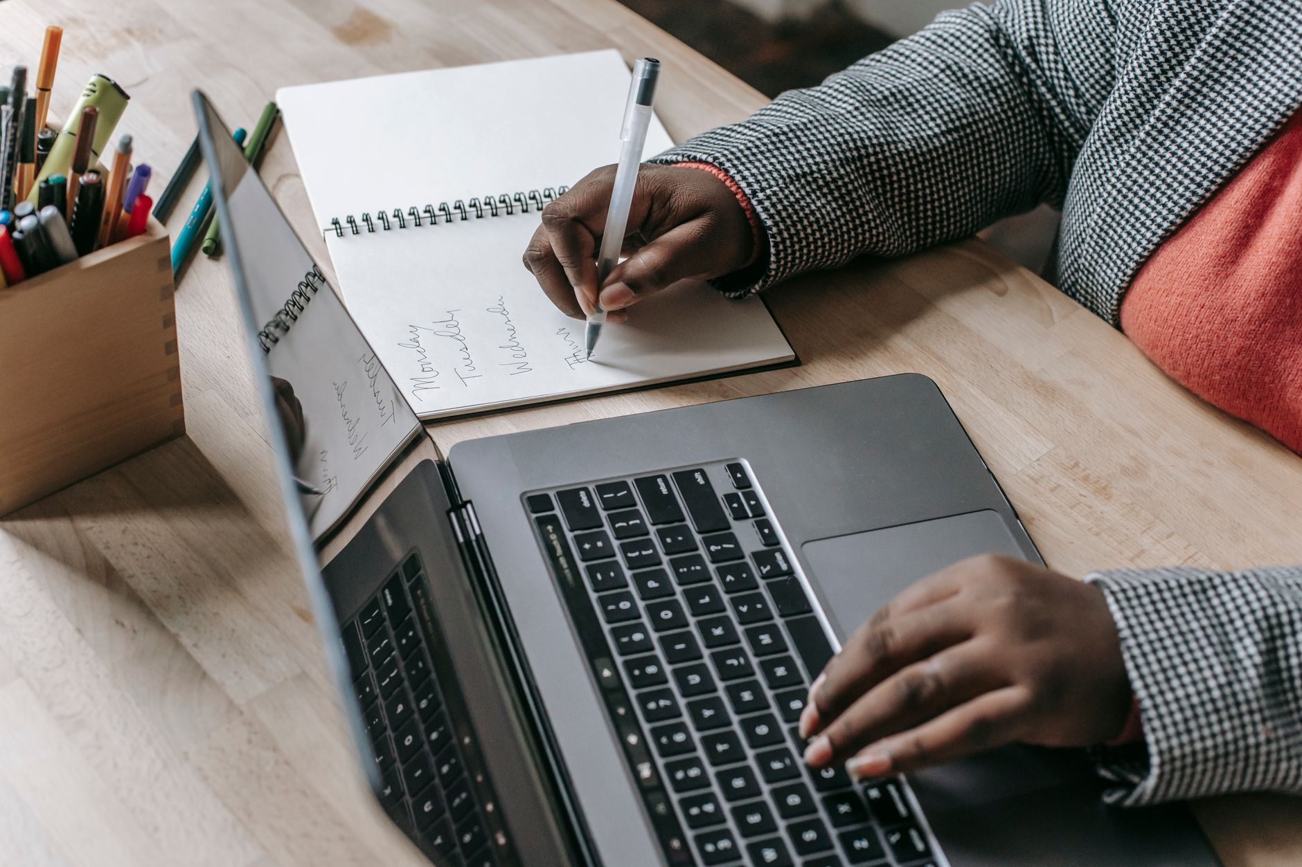 Crop unrecognizable African American female in formal wear writing notes in notepad while working on laptop — The brochure ca