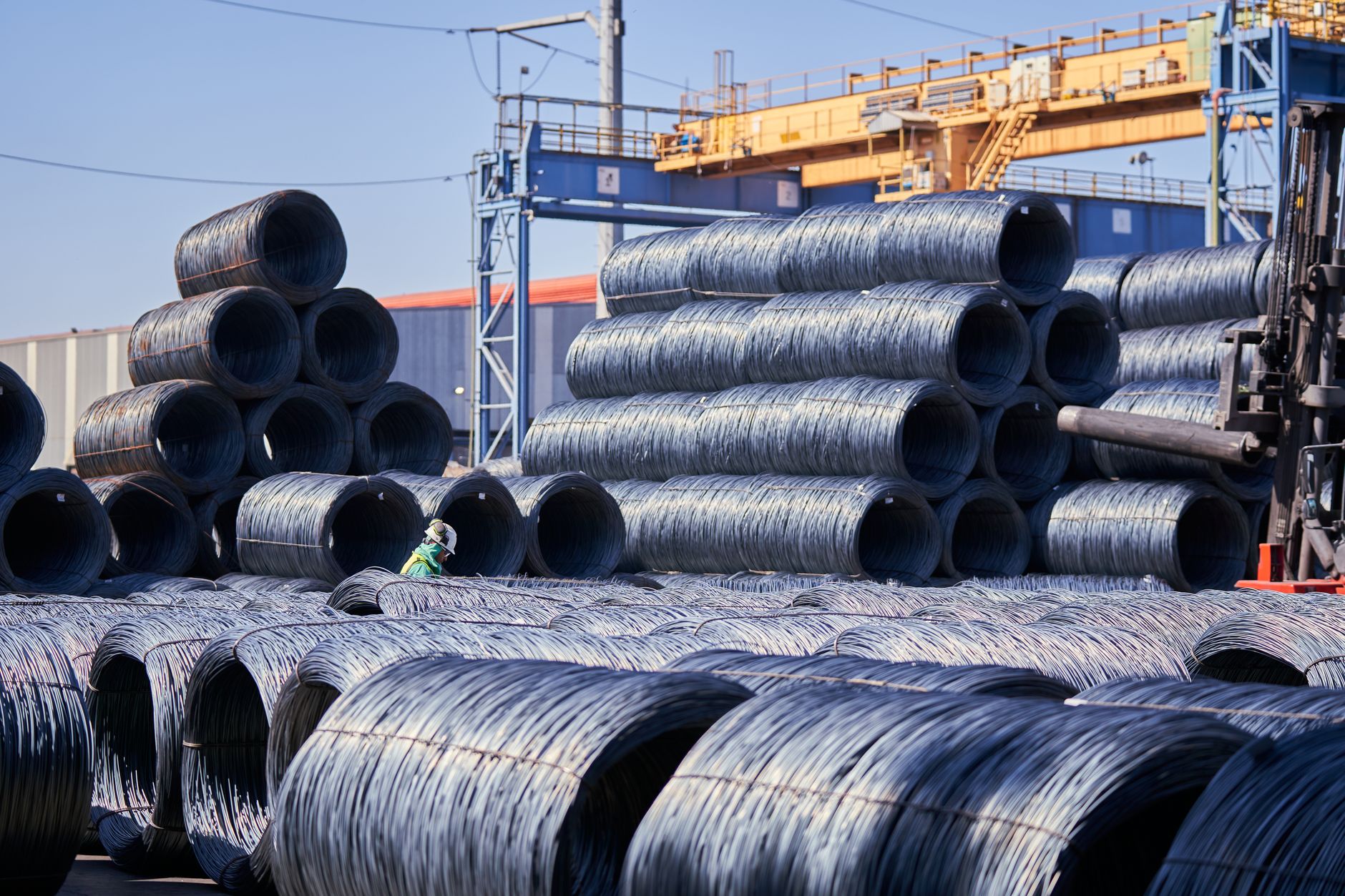Large stacks of steel wire coils stored outdoors at an industrial site under bright daylight. — The Different Applying Indust