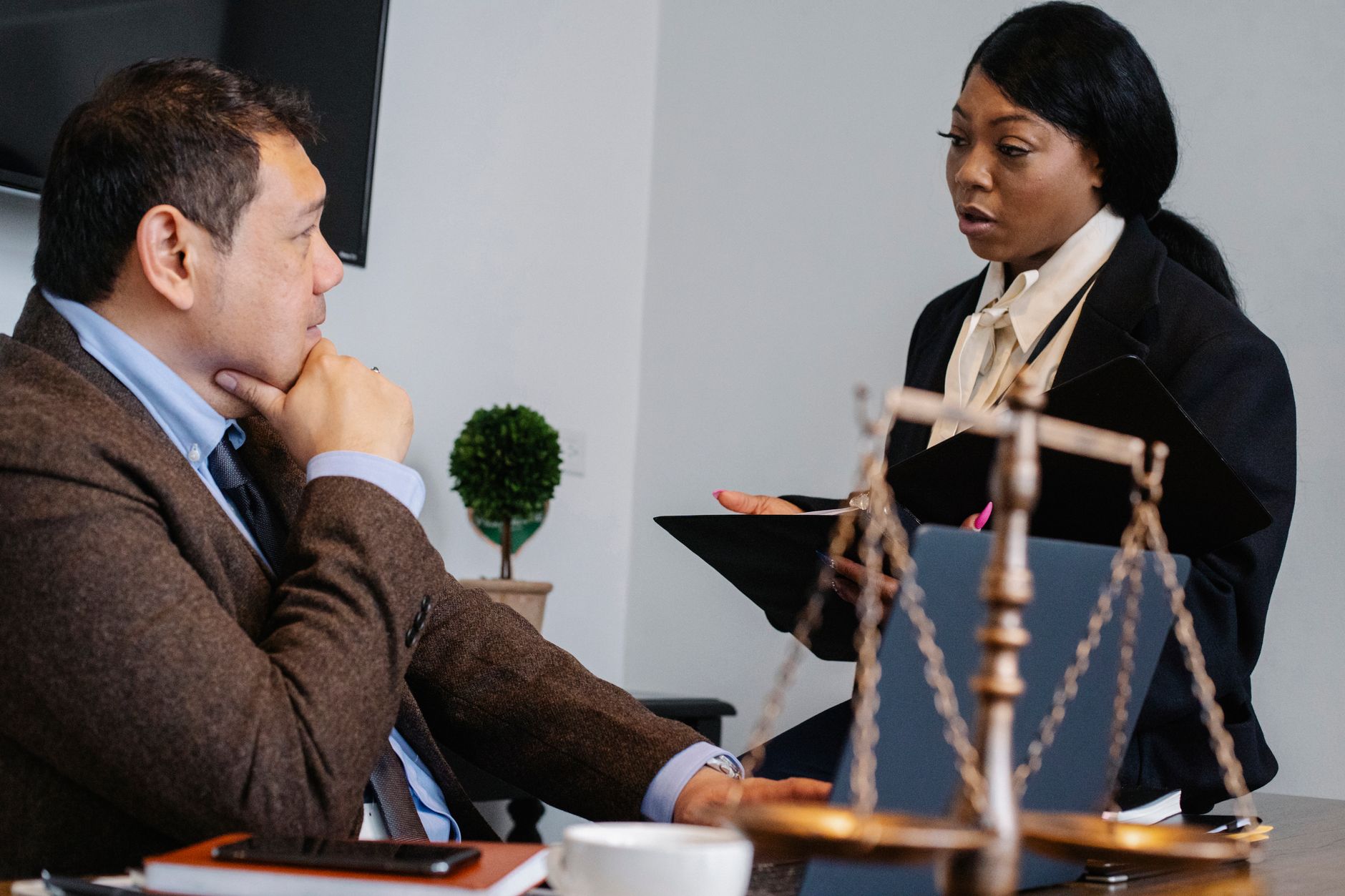Side view of pensive diverse colleagues in formal clothes sitting at table and discussing details of project at work — The Sp