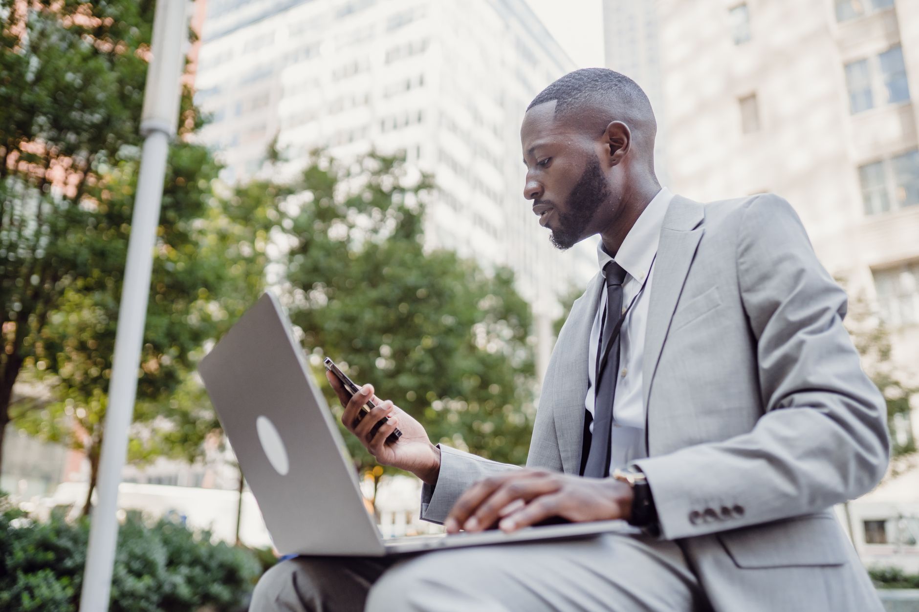 Businessman in a suit using a laptop and smartphone in an urban setting, blending technology with business. — Top Forex Tradi