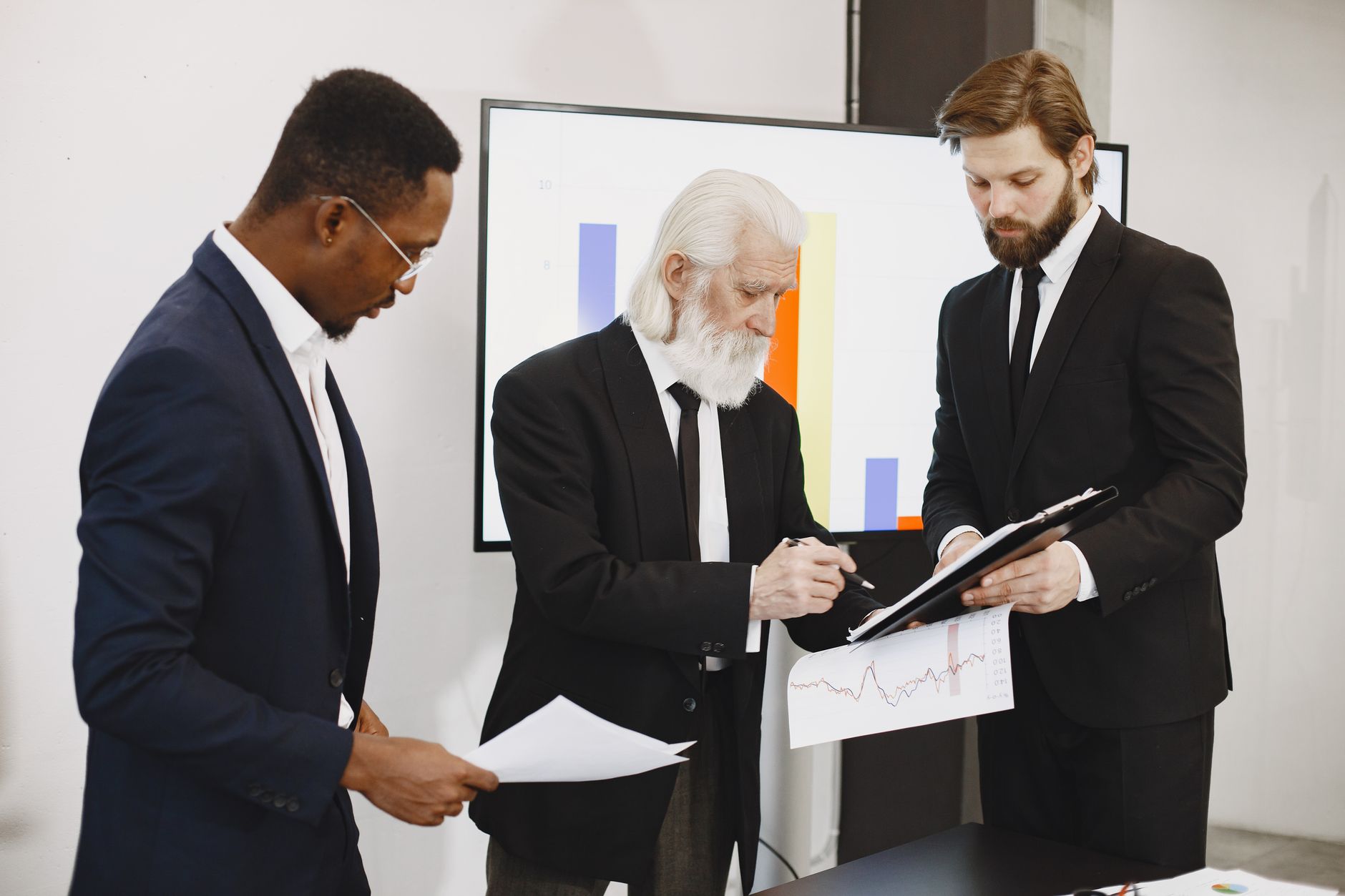 Three businessmen in suits reviewing reports and graphs during an office meeting. — Website an important part of the business