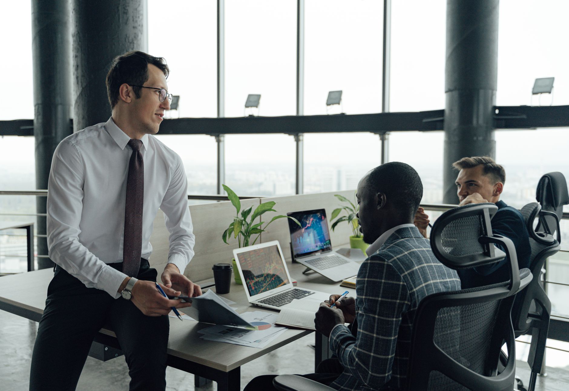 Three men engaged in a business meeting in a modern office setting with laptops and documents. — Workplace accident in Virgin